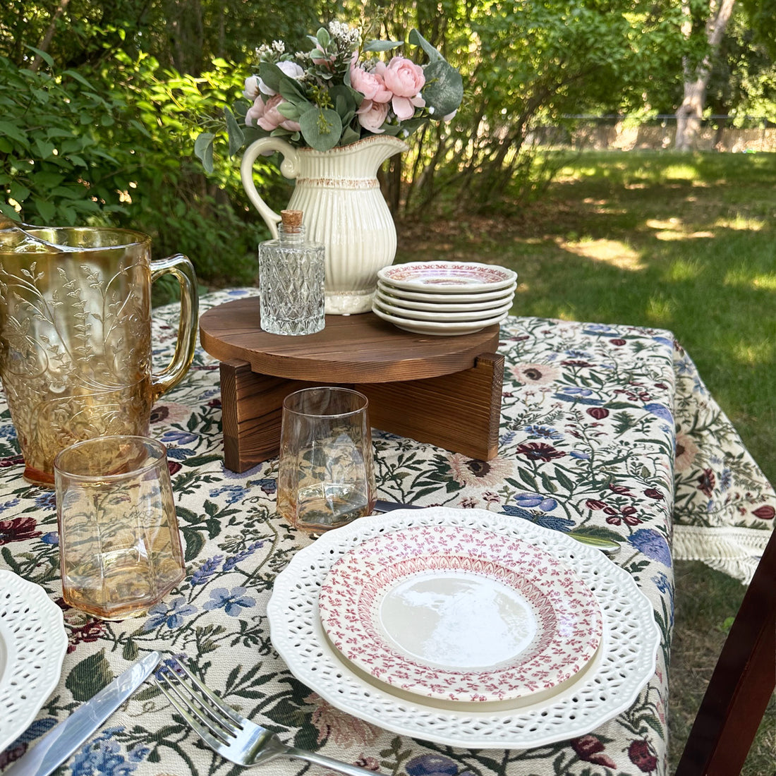 Floral pattern covered table decorated with plates, glasses, and cake stand for blog post on How To Host A Garden Party