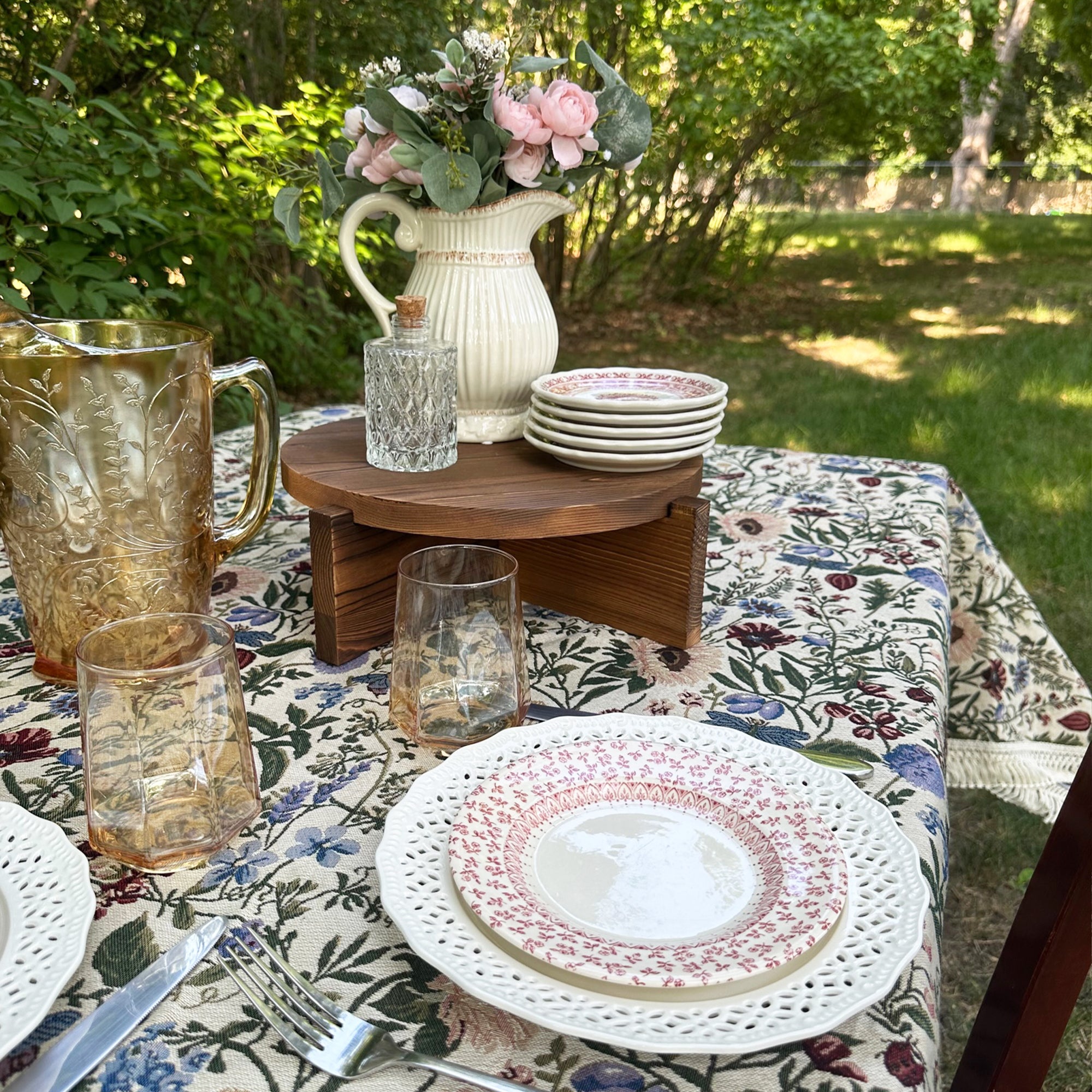 Floral pattern covered table decorated with plates, glasses, and cake stand for blog post on How To Host A Garden Party